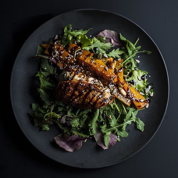 Glazed chicken pieces on a bed of leaves on a dark plate